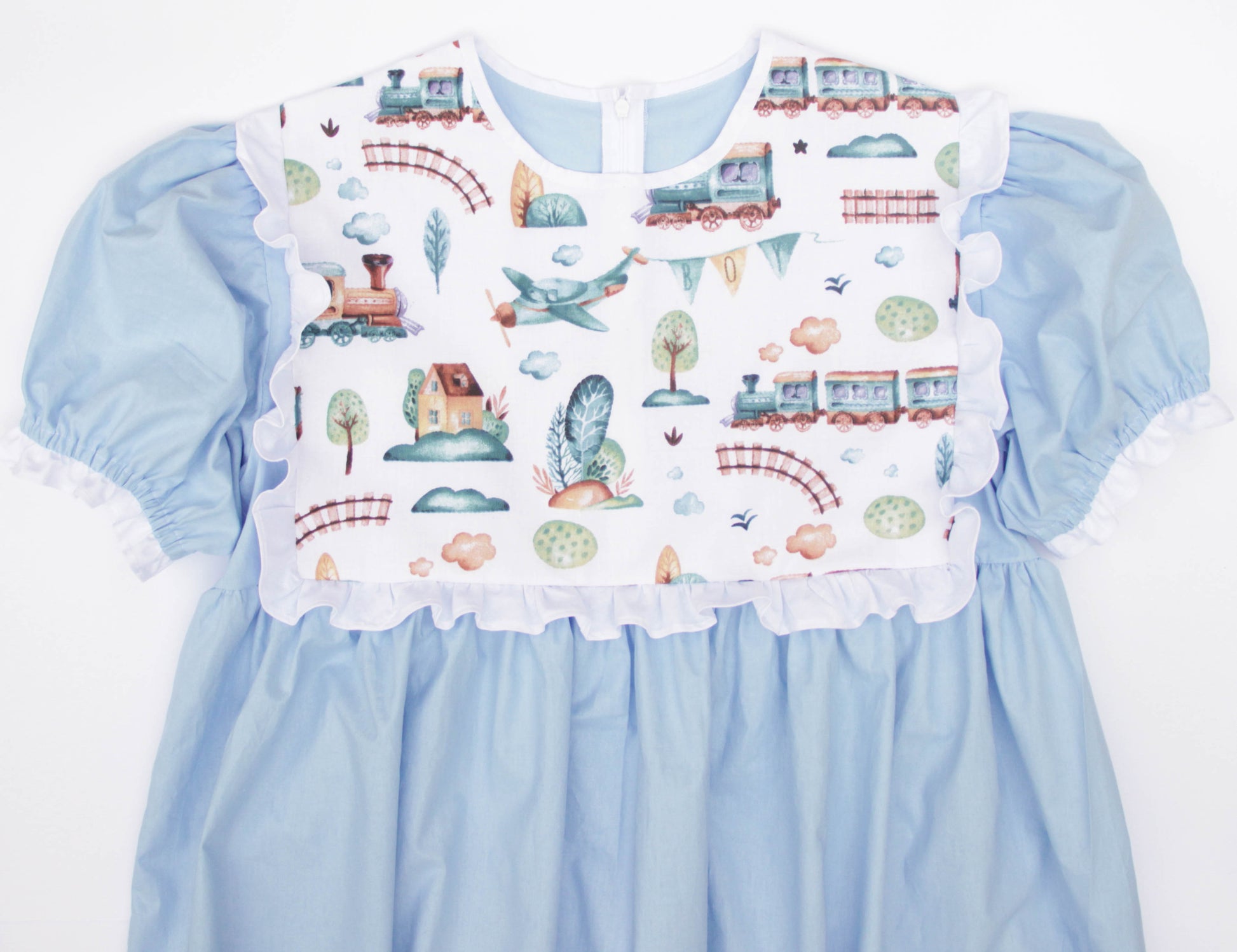 Light blue dress with a white bib featuring transportation-themed print on a white background